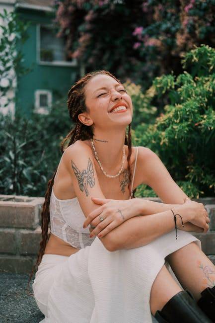 每日三問，啟動感恩顯化
Smiling woman with tattoos and braids, sitting relaxed in a garden.